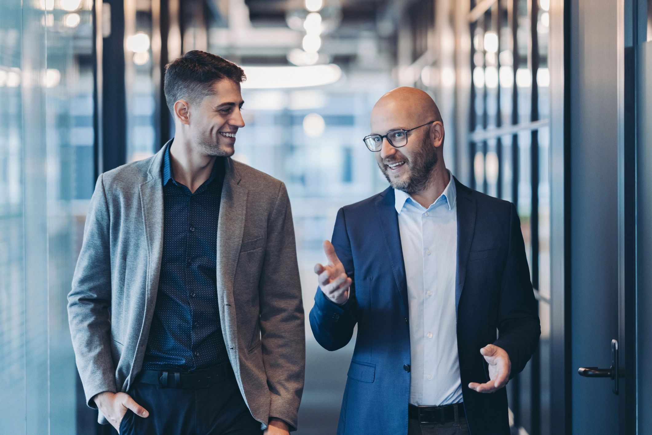 Two colleagues in conversation while walking through an architectural corridor